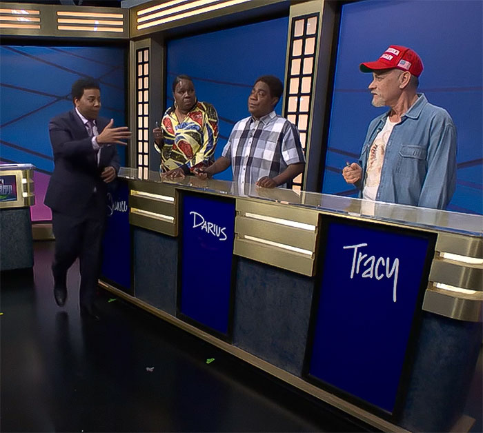 A game show scene with actors, one in a MAGA hat, behind a podium labeled "Tracy," participating in a skit.