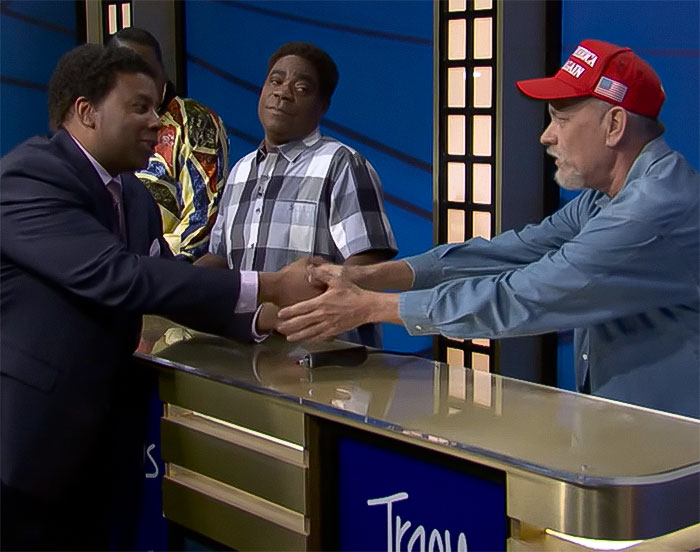 Actors in a game show skit, one wearing a MAGA hat, shaking hands across a table on a studio set.