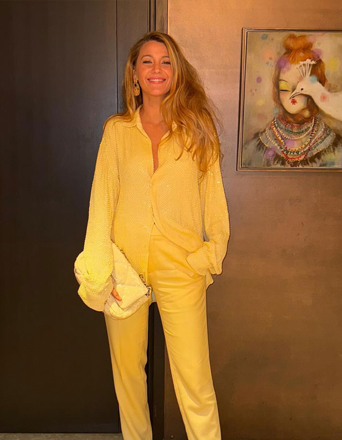 Blake Lively in a yellow outfit, smiling and posing indoors, with wall art in the background.