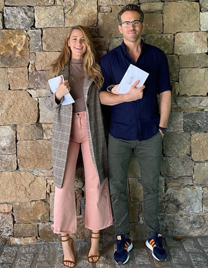 Two people standing against a stone wall, holding notebooks, related to Justin Baldoni's behavior during scenes.