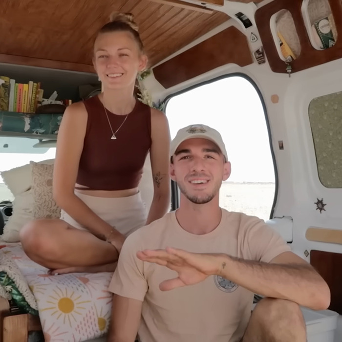 Young couple sitting in a van interior, smiling at the camera, related to Brian Laundrie and Gabby Petito story.