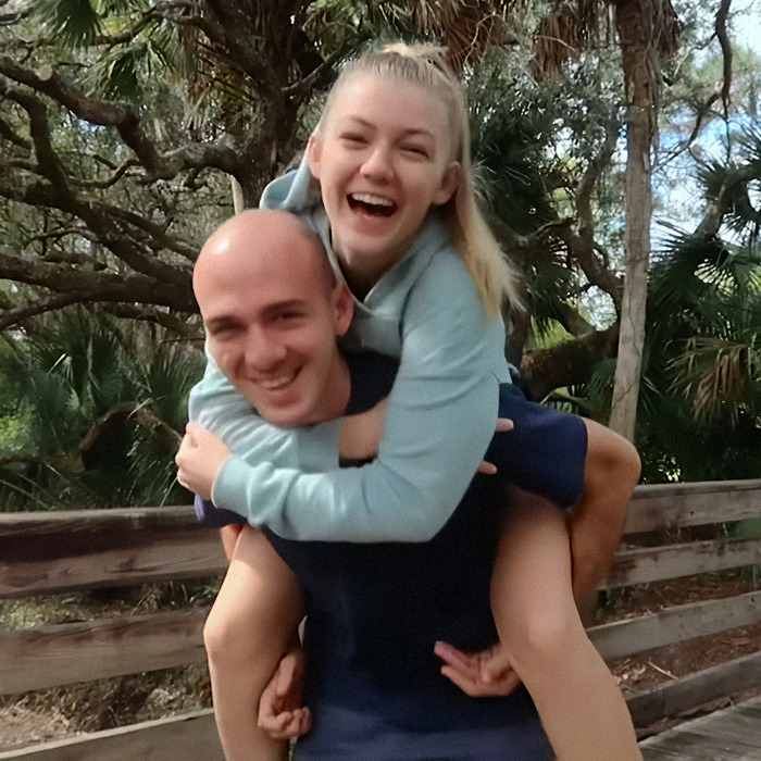 A man giving a woman a piggyback ride on a wooded path, smiling and joyful.