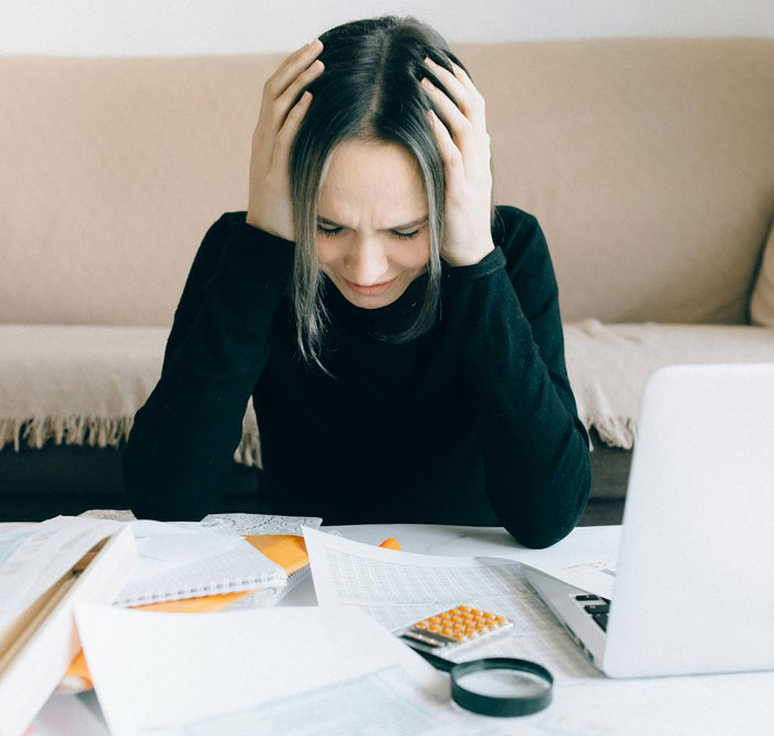 Stressed woman with hands on head at desk, surrounded by paperwork, seeking refunds after wedding didn&rsquo;t work out.