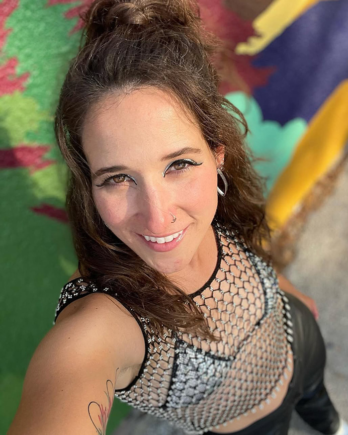 Woman smiling outdoors, associated with viral misgendering incident, wearing a netted top.