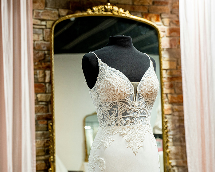 Wedding dress with lace details on a mannequin in front of a mirror, highlighting bridal fashion choices.