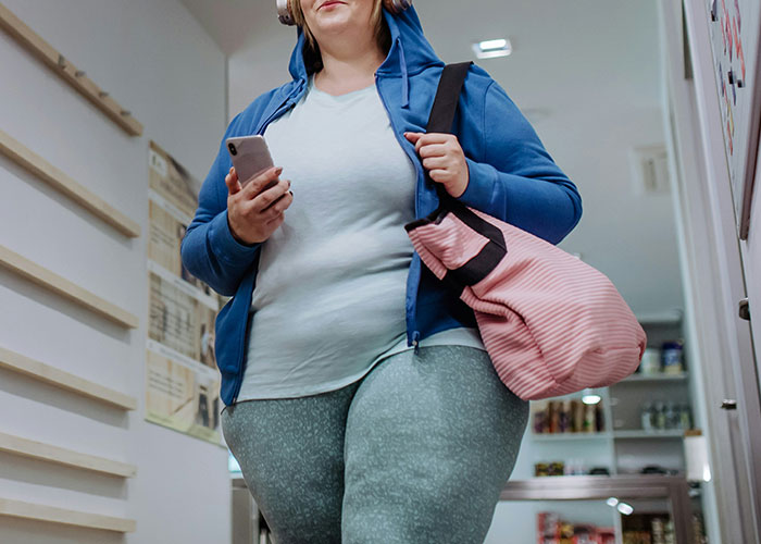 Woman in workout clothes holding a phone and bag, related to health and weight discussion.