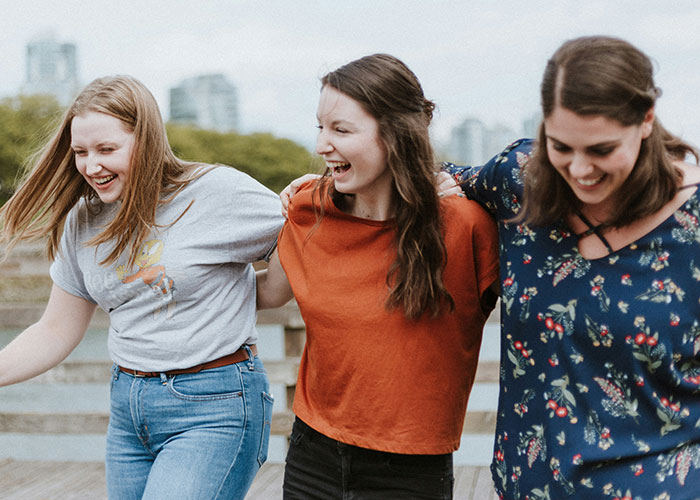 Three friends laughing and walking outdoors, highlighting friendship dynamics and health conversations.