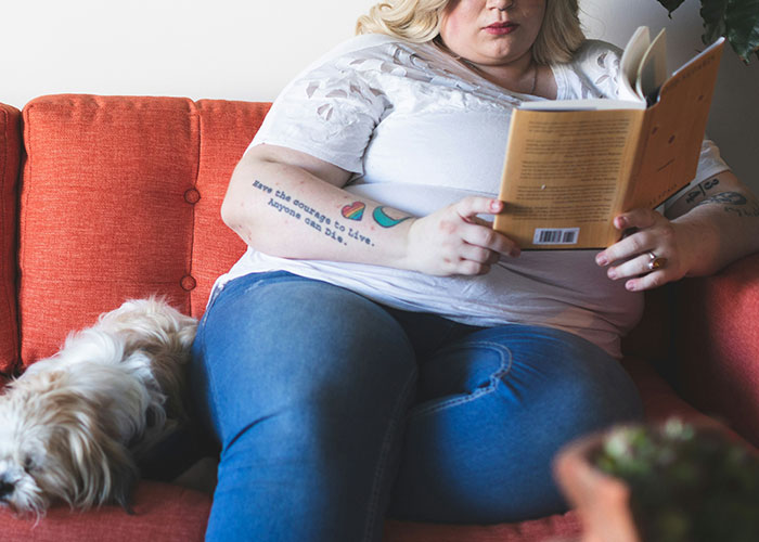 Woman reading on a couch with a dog, related to conflict over health and weight.