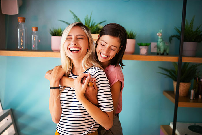 Two women smiling in a cozy room, reflecting joy and togetherness amidst plants and home decor.