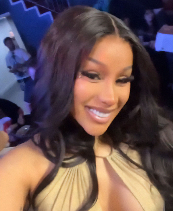 A woman taking a selfie at a Superbowl party, smiling brightly with long hair and a beige outfit, capturing joyful reactions.