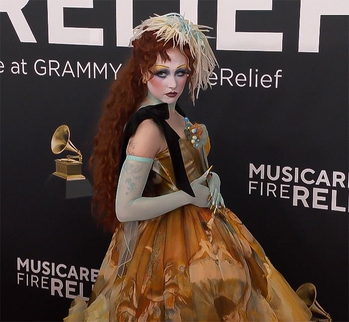 Chappell Roan at a Grammy event wearing a colorful dress, posing in front of a backdrop with music symbols.