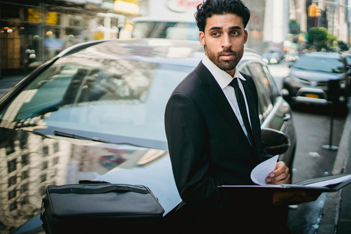 A professional man in a suit stands by a car on a city street, representing professions with more cheaters.