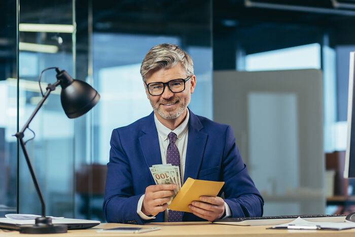 Man in a business suit counting money at his desk, highlighting professions with higher rates of infidelity.