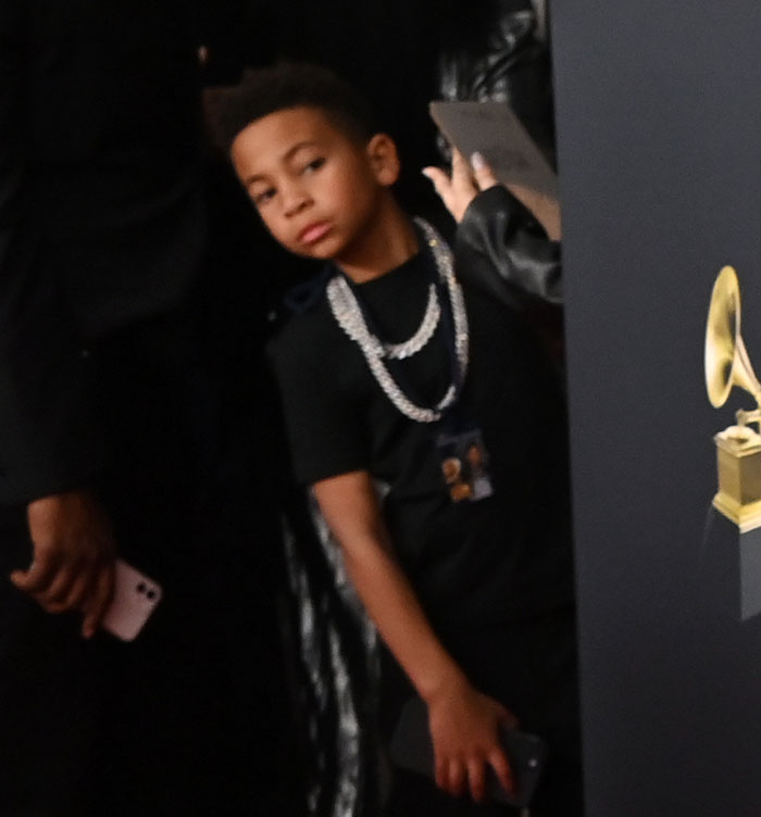 Child at the Grammys red carpet, glancing sideways, wearing a black outfit and silver chain.