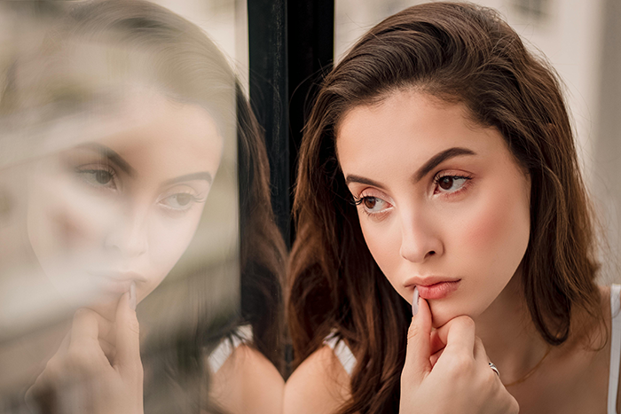 A thoughtful woman looking out of a window, illustrating the dilemma of a child-free couple considering a vacation.