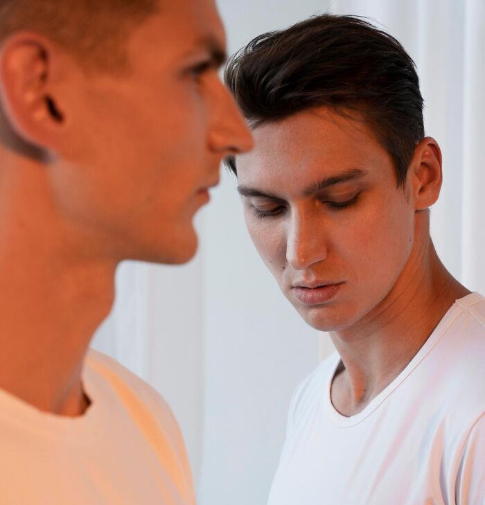 Two men in white shirts standing close together, one looking away, depicting awkward first date scenario.