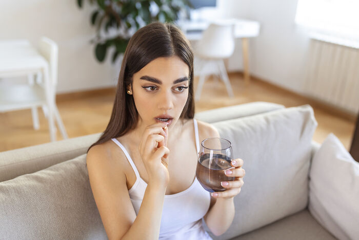 Woman on a couch holding a glass of water, contemplating a pill, representing travel must-haves for packing.