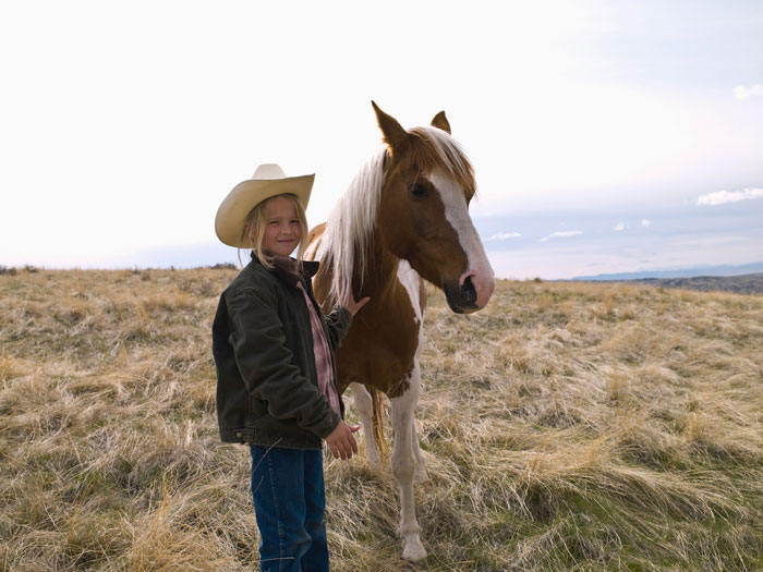 Child in cowboy hat with horse in open field.