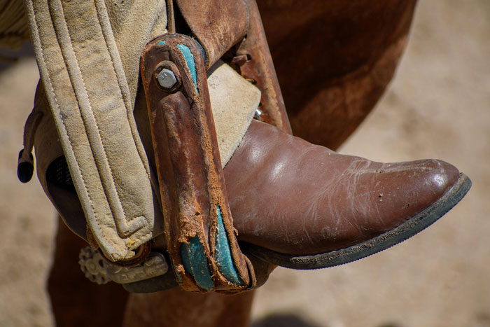 A brown cowboy boot in a stirrup, highlighting the unique function of cowboy boots on fences.