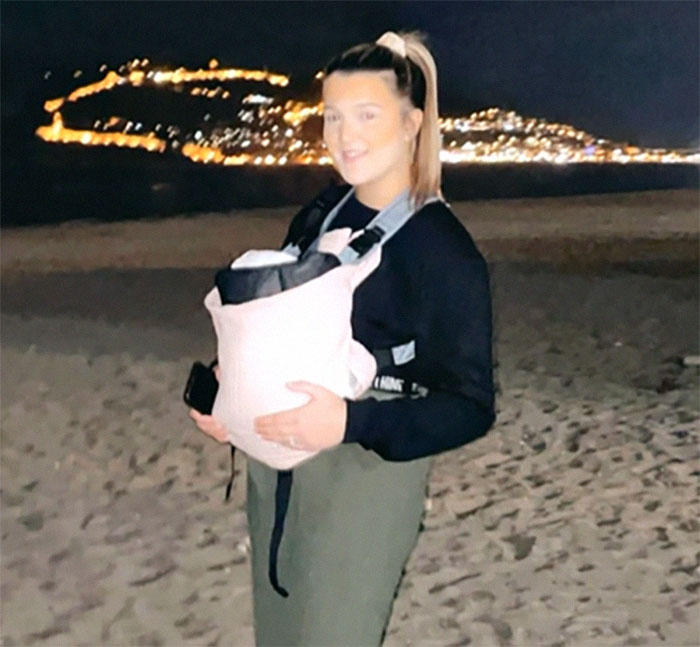 Teen with baby carrier on beach at night, city lights in background, related to medical case from 1988.