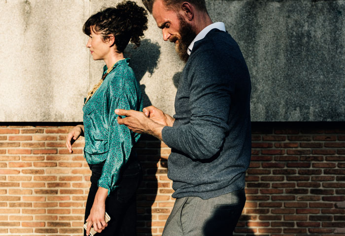 Man and woman walking outdoors, both looking at their phones, depicted as dad and his girlfriend in urban setting.