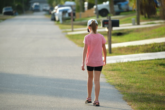 Teen girl in pink shirt walking down a suburban street, summer afternoon.