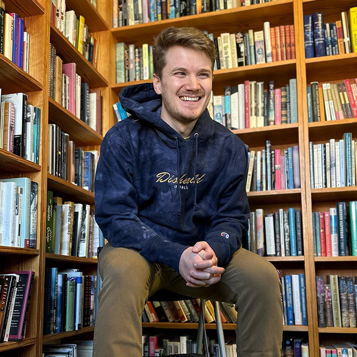 Person in a cozy library, wearing a dark hoodie, surrounded by shelves filled with bookshelves, related to BookTube crisis.