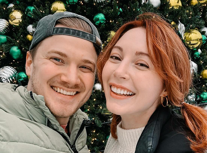 Happy couple smiling in front of a decorated Christmas tree, related to BookTube crisis.