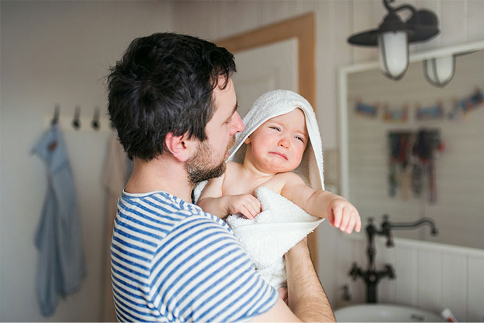 Father struggles to calm crying infant in towel, reflecting drama over parental responsibilities.