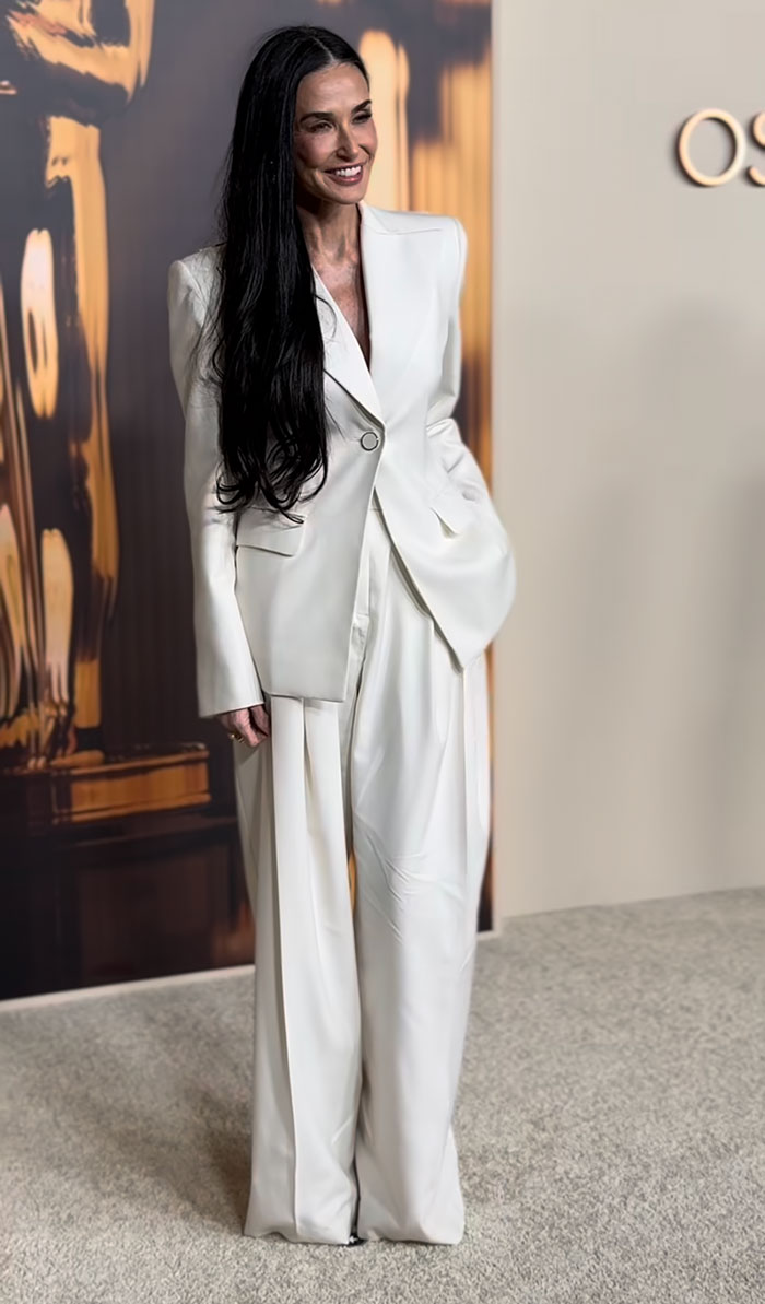 A woman in a sleek white suit at the 2025 Oscar Nominees Dinner, showcasing a fashion triumph.