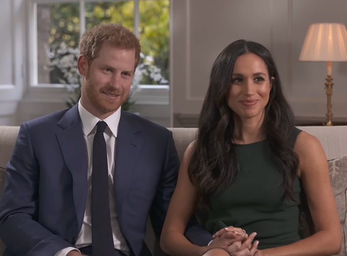 Meghan Markle and Prince Harry sitting together in a living room, smiling, wearing formal attire.