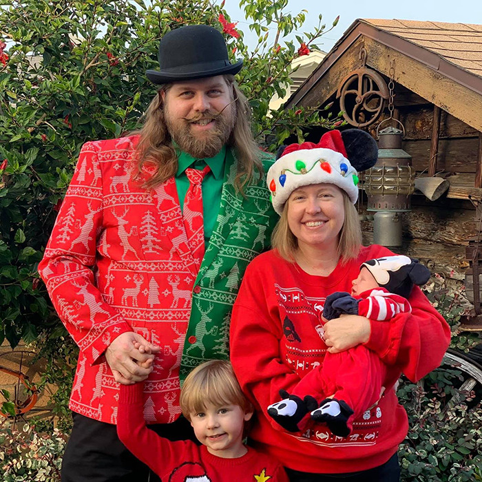 Matthew Van Andel in festive attire with family, including colorful holiday sweaters and hats, posing outdoors with Disney-themed decorations.