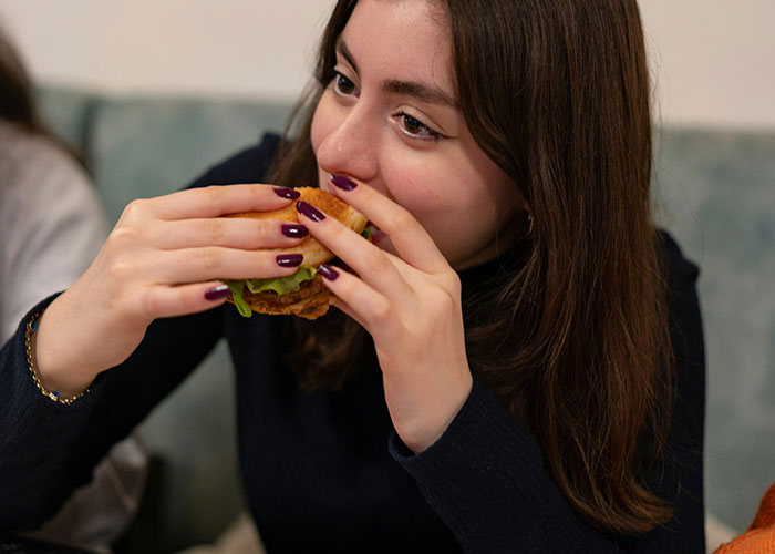 Woman with long hair eating a burger, illustrating being late to a job.