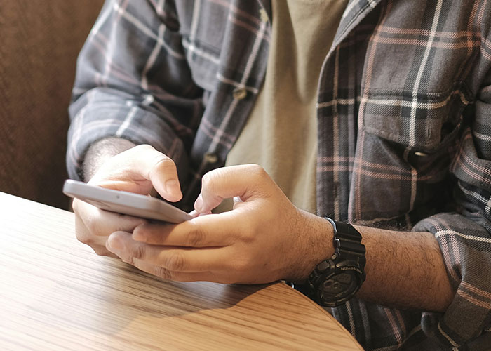 Man checking phone, wearing a plaid shirt, related to getting girlfriend a job.