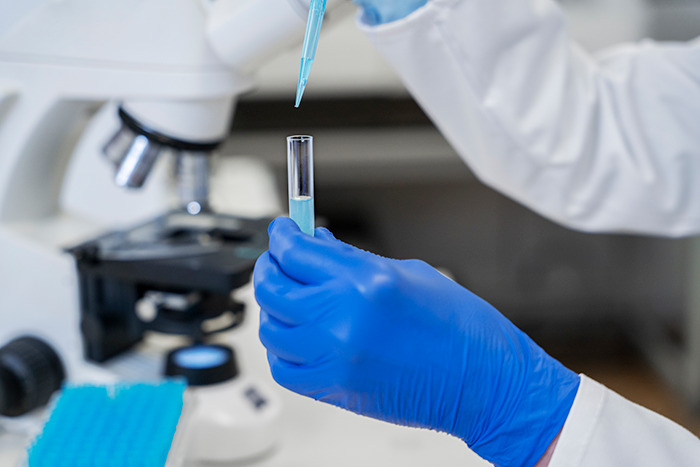 Lab technician using DNA testing equipment, holding a pipette and test tube, related to Jack the Ripper investigation.