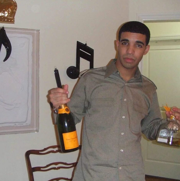 Drake holding champagne and liquor bottles in a room with musical decor, relating to net worth themes.