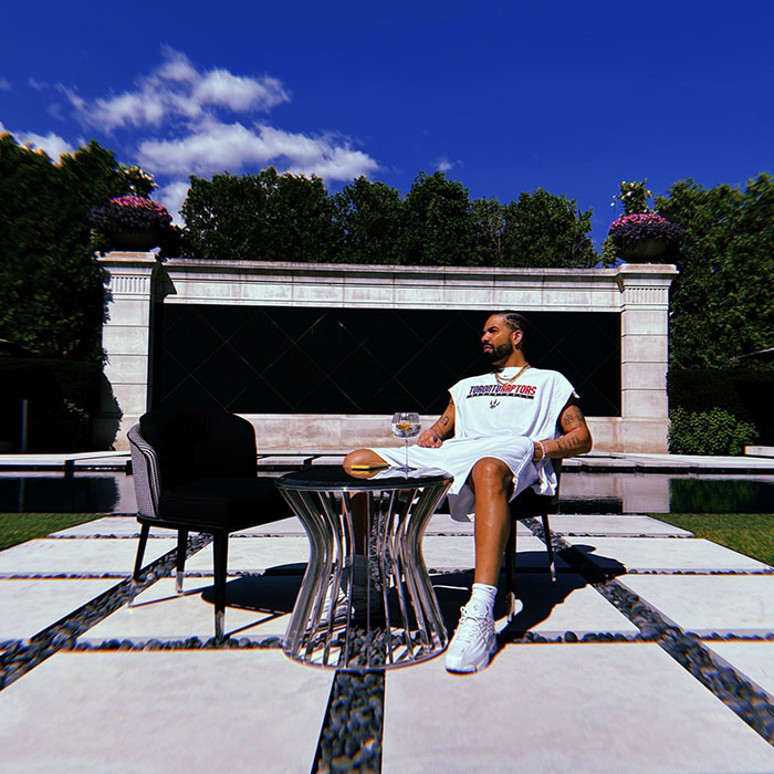 Drake relaxing outdoors, wearing a Raptors shirt, near a table with a drink, illustrating elements of Drake\'s net worth lifestyle.