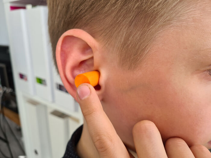 Person inserting an orange earplug, highlighting travel must-haves for a better packing experience.