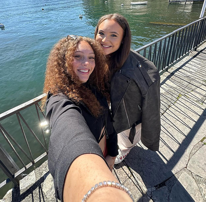 Two young women smiling by a scenic lake. New influencer, 24, enjoying a sunny day outdoors.