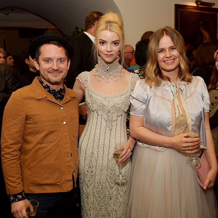 A group of people at a formal event, one person wearing a brown jacket, smiling, holding a drink.