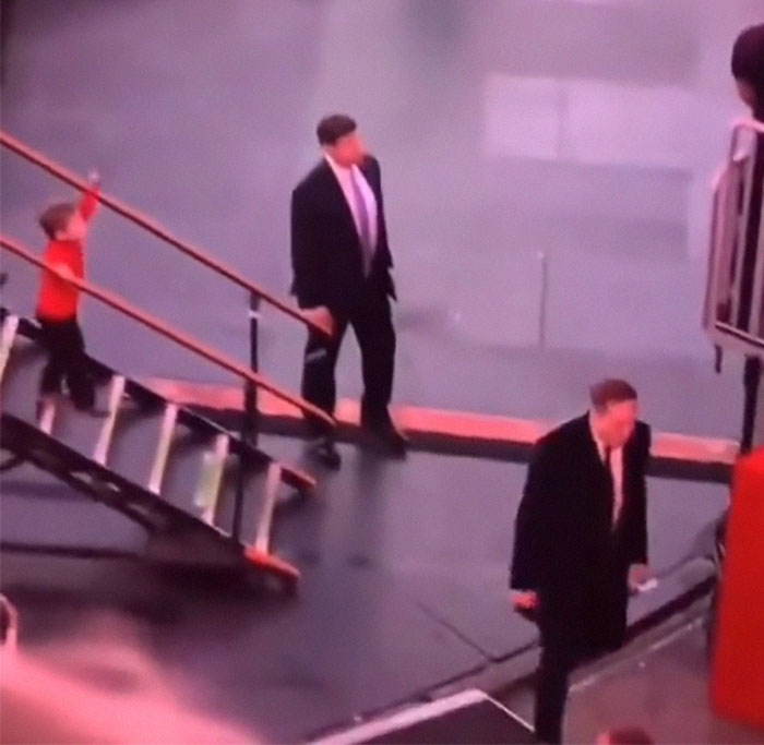 Elon Musk walking away from son X Musk on stairs, in a formal setting