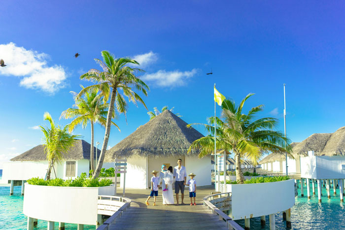 Family vacation at a tropical resort with overwater villas and palm trees under a clear blue sky.