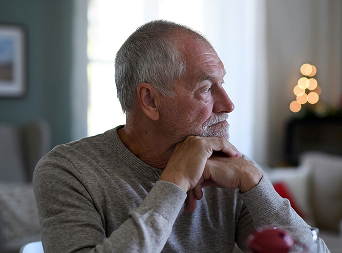 A thoughtful single dad in a grey sweater, sitting at a table, contemplating a decision.