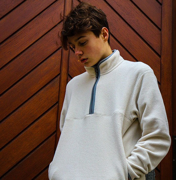 Teen in white fleece stands thoughtfully against a wooden backdrop, representing son's best friend context.