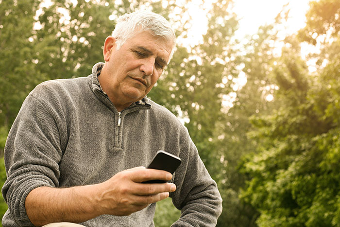 A single dad in a grey sweater looks at his phone thoughtfully outdoors.