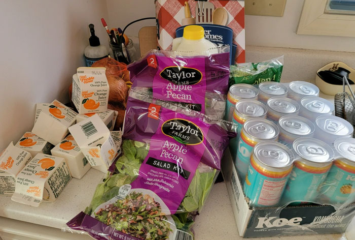 Food bank items: salad kits, orange juice boxes, and canned drinks on a kitchen counter.