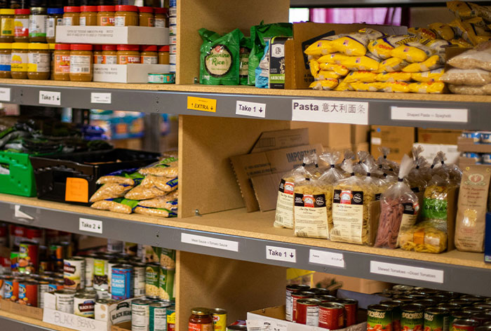 Food bank shelves stocked with canned goods, pasta, and rice, highlighting community support and volunteer opportunities.