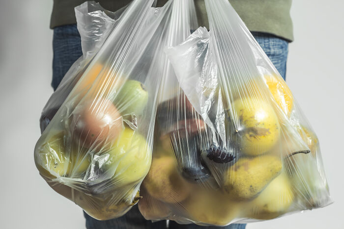 Person carrying two plastic bags full of assorted fruits.