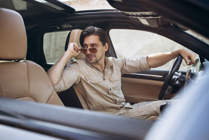 Man in sunglasses confidently seated in a car, appearing thoughtful, representing theme of food bank and income deception.