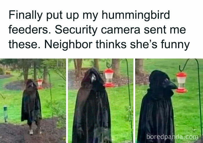 Person dressed as a crow, resembling a "final boss," next to a hummingbird feeder in a garden, captured by a security camera.